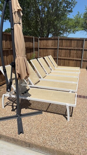 Una hilera de tumbonas con dosel, frente a un fondo de valla de madera.