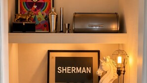 Een compact keukenhoekje met een geïntegreerde wijnkoeler, een houten snijplank, een ingelijst bord en een decoratief paardbeeld.