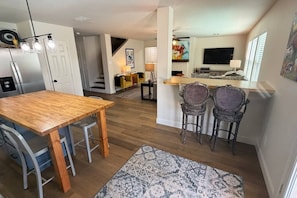 Eine moderne Küche mit Holztisch und Barhocker, einer Treppe und einem Wohnbereich mit Fernseher und Kunstwerken.