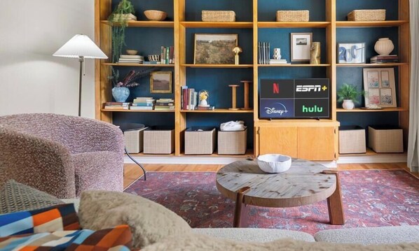 Un salón con sofá, una mesa de centro, una estantería y un mueble para televisor mostrando servicios de transmisión.