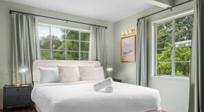 Un dormitorio bien iluminado con una cama grande, dos mesitas de noche y una ventana con cortinas.