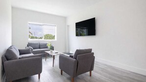 Una sala de estar moderna con un sofá gris, dos sillones, una mesa de centro y un televisor de pantalla plana montado en la pared.