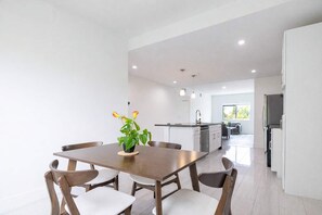 A modern kitchen with white cabinets, a central island, and a dining area with a wooden table and chairs. - Comfortable 3BR • 4 Beds • Parking Included (Hallandale Beach)