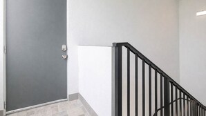 Una puerta cerrada con manija metálica, una barandilla de escaleras de metal negro y una pared blanca.