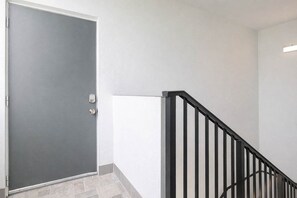 A closed door with a metal handle, a black metal staircase railing, and a white wall.