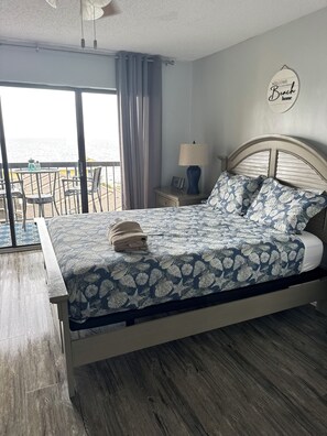 Ein Schlafzimmer mit Bett, Nachttisch, Lampe und Meerblick, sowie einem Schild mit der Aufschrift 'Welcome to our Dream Beach home'.