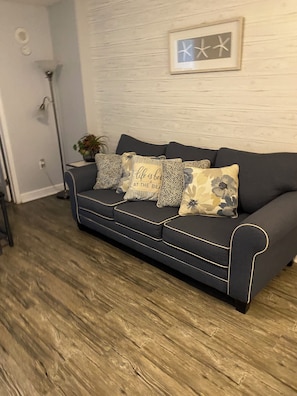 Ein dunkelblaues Sofa mit gemusterten Kissen, Holzboden und eine an der Wand befestigte Uhr.