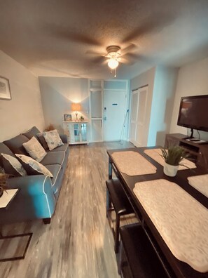 Ein modernes Wohnzimmer mit einer Couch, einem Esstisch, einem Deckenventilator und einem Fernseher.