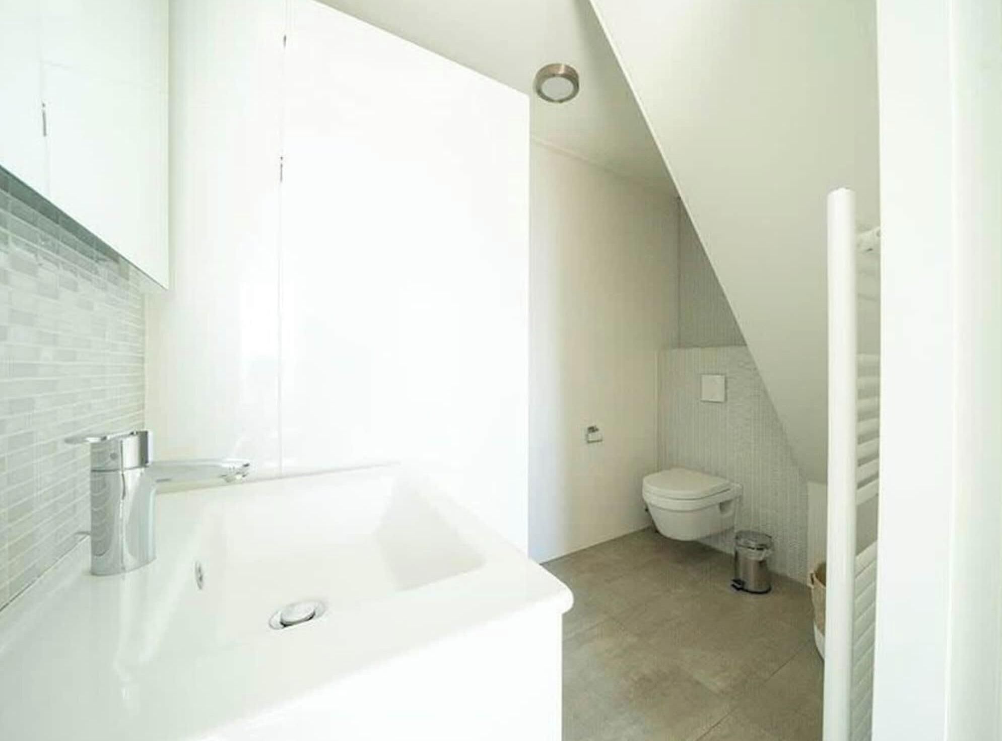 A modern bathroom with a white sink, a toilet, and a shower area.
