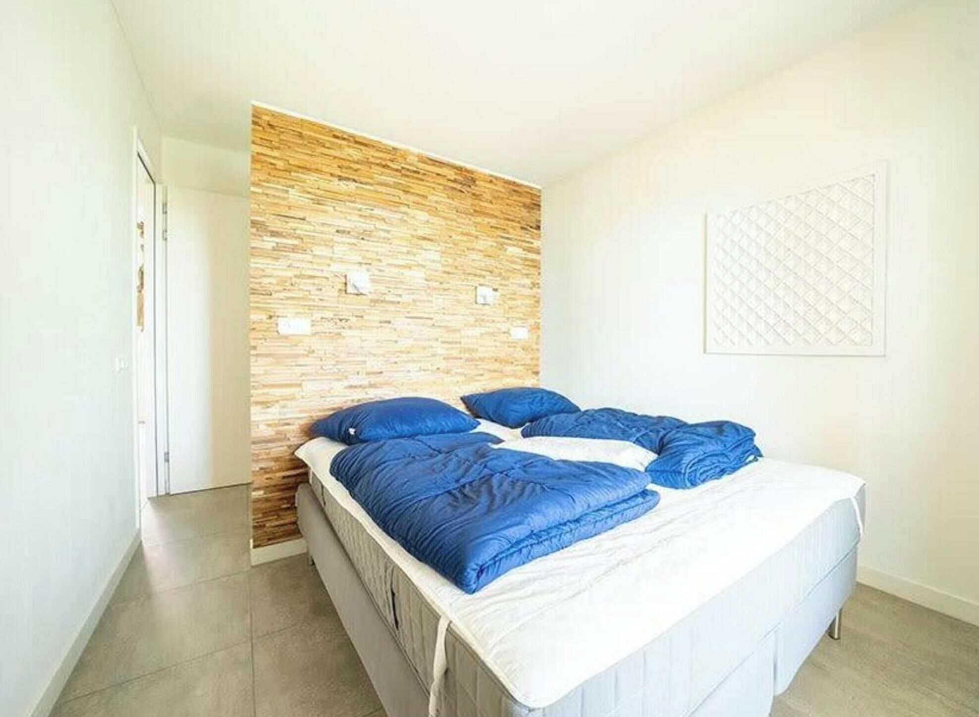 Quarto com cama, cabeceira de madeira e parede branca com design estampado.