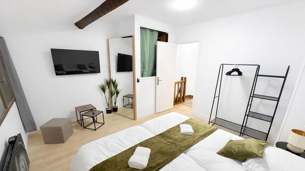Ein Hotelzimmer mit Bett, Fernseher, Spiegel, kleinem Tisch, Stuhl, Pflanze und Kleiderschrank.