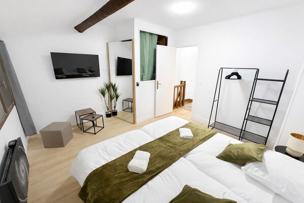 A hotel room with a bed, a TV, a mirror, a small table, a chair, a plant, and a wardrobe.
