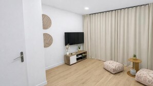 Ein modernes Wohnzimmer mit Flachbildfernseher, Holzboden, einer Couch, einem kleinen Beistelltisch und einem Vorhang.