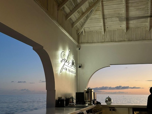 Decoración con temática náutica, un letrero que dice 'Sydney's on the Rockis', vista al mar y una zona de bar con equipamiento.