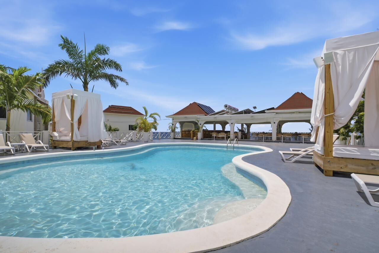 A pool with clear water, surrounded by lounge chairs and covered seating areas.