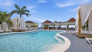 A pool with clear water, surrounded by lounge chairs and covered seating areas.