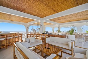 A spacious outdoor lounge area with wooden furniture, white sofas, and a thatched roof. - Sunkissed Ocean Front Suite at The West Signature (Negril)