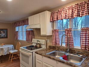 A kitchen with a stove, sink, and window with checkered curtains.