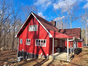 Une maison en bois rouge, avec un porche, une cheminée et un ciel dégagé.
