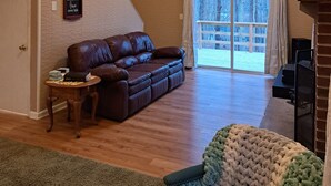 Un salon spacieux avec un canapé en cuir marron, une petite table d’appoint en bois, un plaid vert en tricot et un ventilateur de plafond.