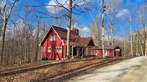 Une grange rouge avec un toit à pignon, entourée d’un sol et d’arbres couverts de feuilles.