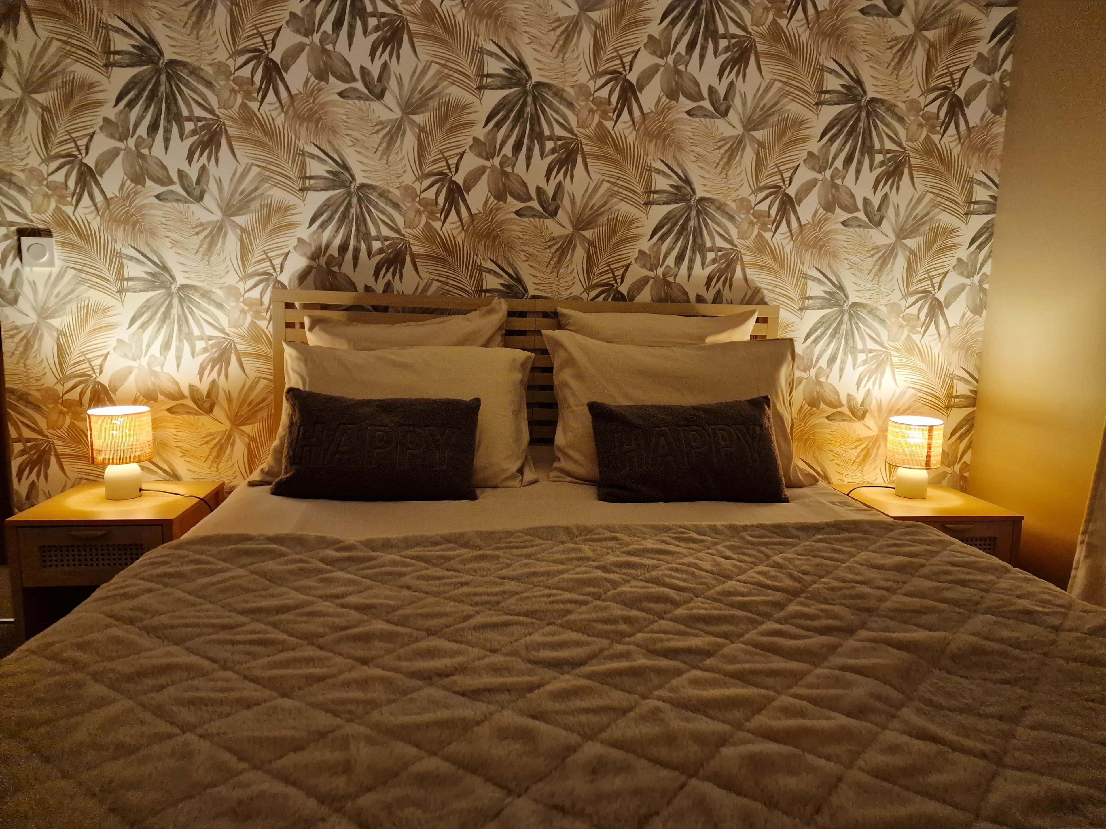 A bed with a quilted cover, two bedside lamps, and a wall with a leaf pattern.