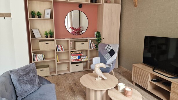 Ein modernes Wohnzimmer mit einem grauen Sofa, einem runden Couchtisch, einem Fernseher und einem Bücherregal mit verschiedenen Gegenständen.