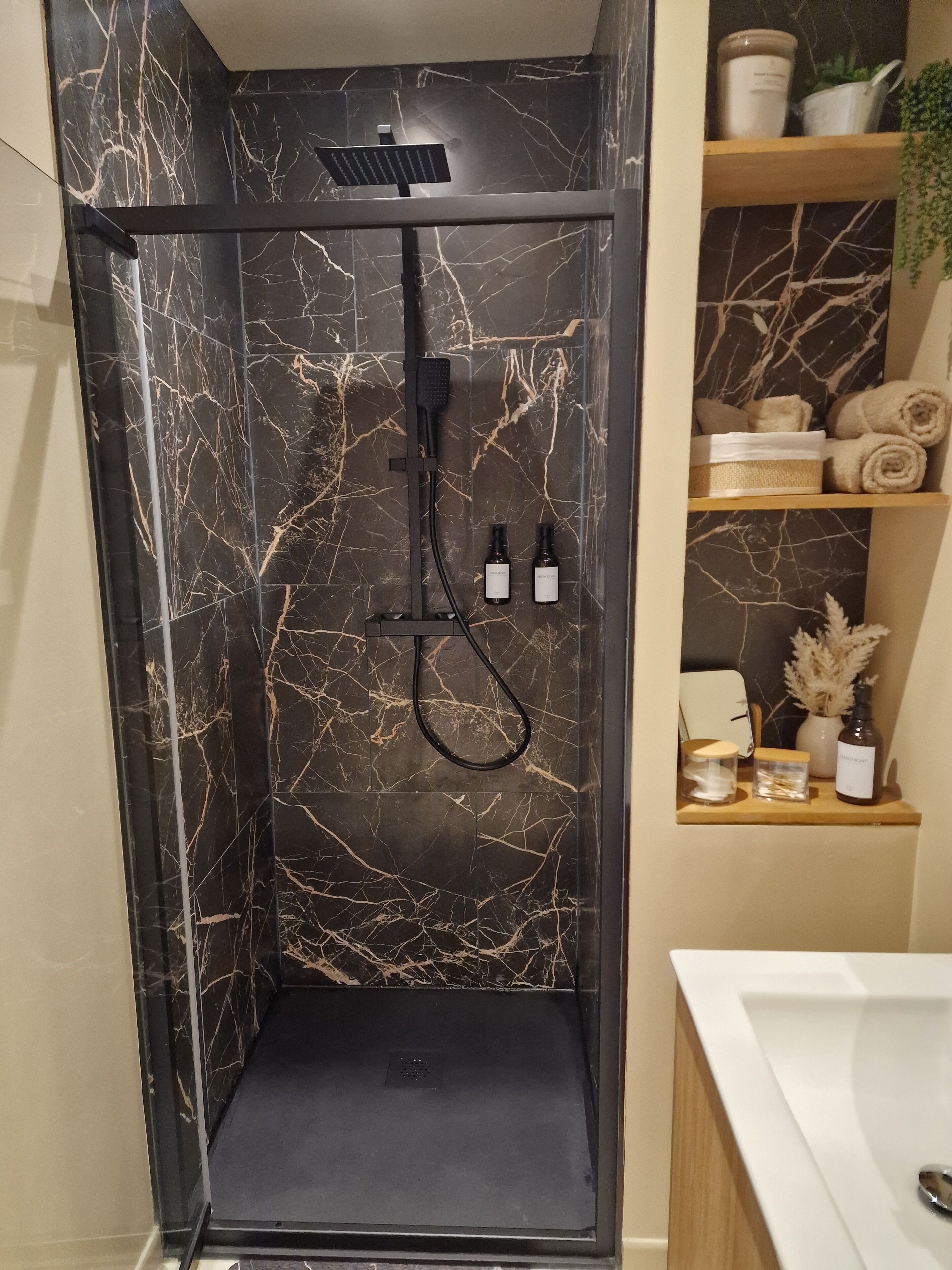 Une cabine de douche avec un revêtement en marbre noir et une douchette à main.