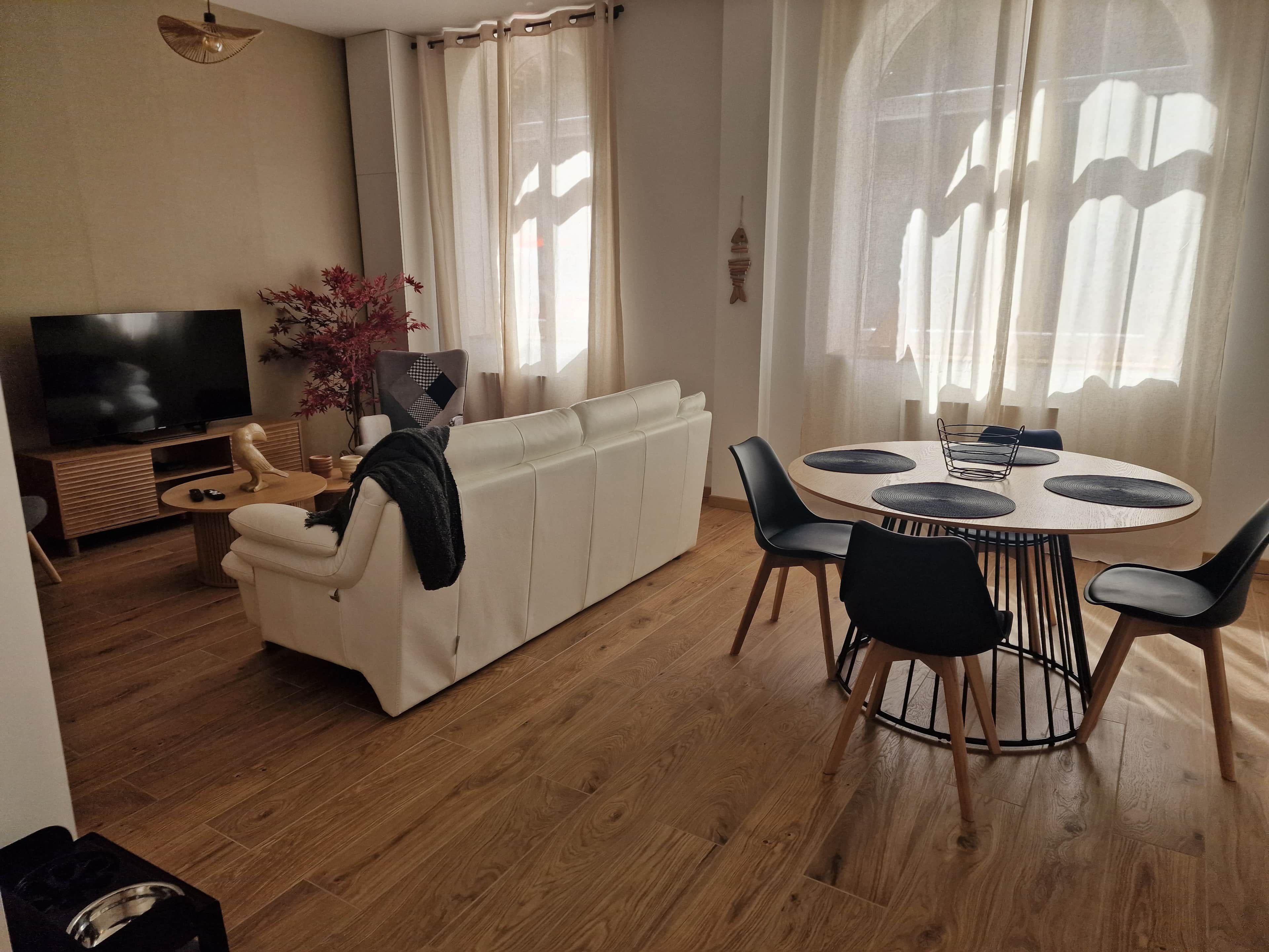 A modern living room with a sofa, TV, dining table, and chairs.