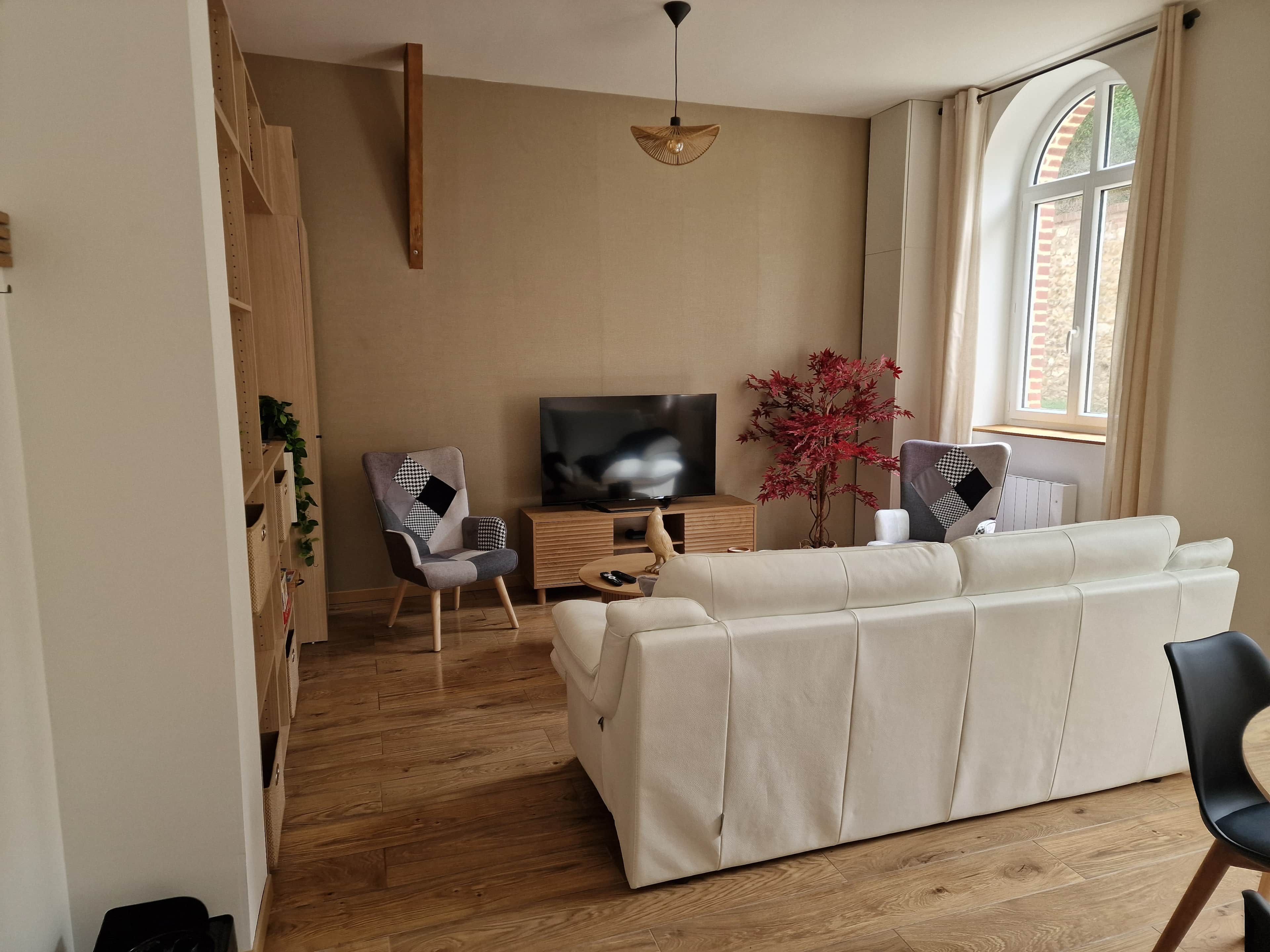 Ein Wohnzimmer mit einer Couch, einem Fernseher, einer Holzkommode und einer Pflanze.