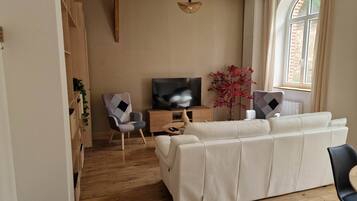 Ein Wohnzimmer mit einer Couch, einem Fernseher, einer Holzkommode und einer Pflanze.