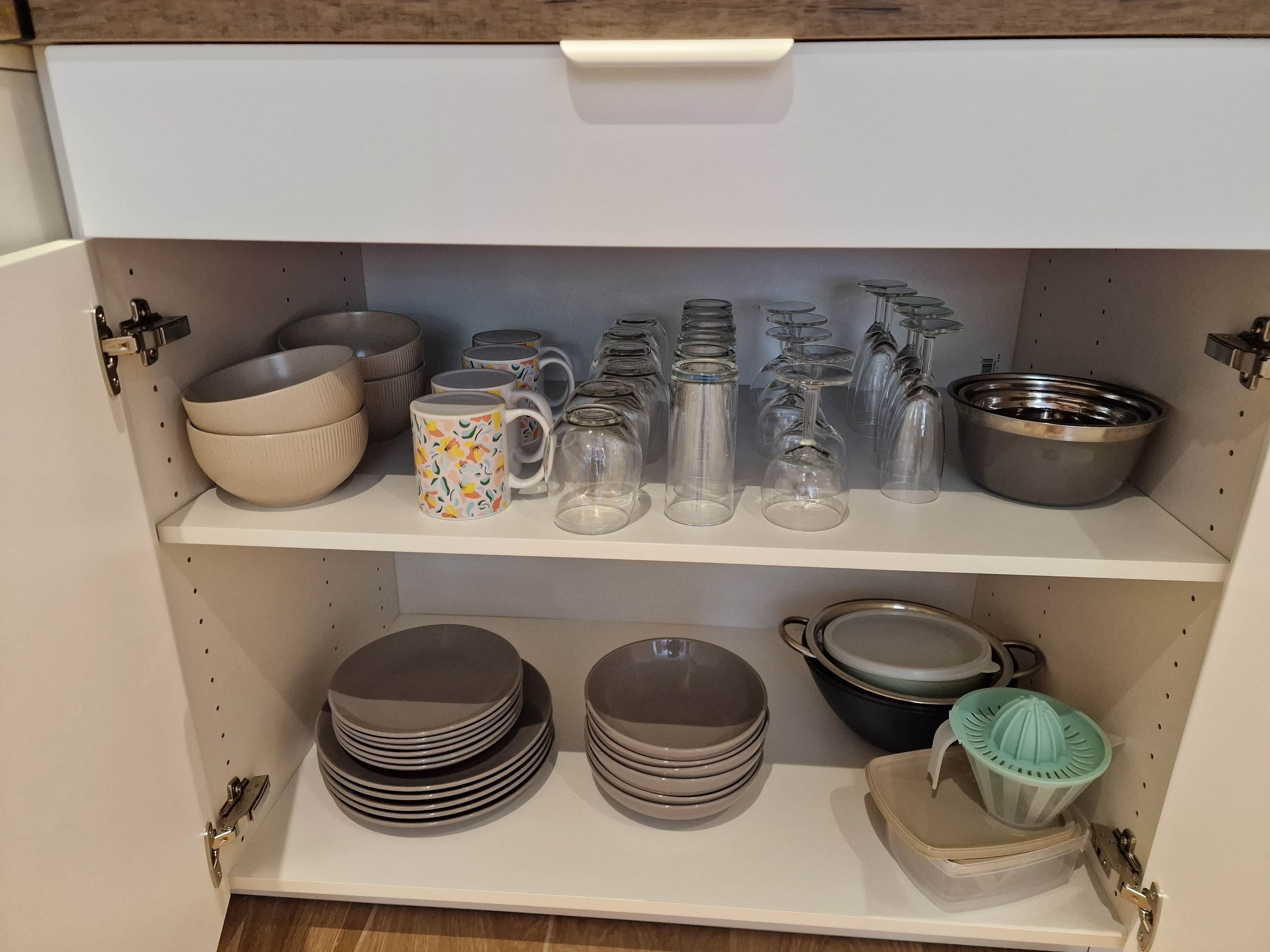 A kitchen shelf with various kitchenware including bowls, mugs, and glassware.