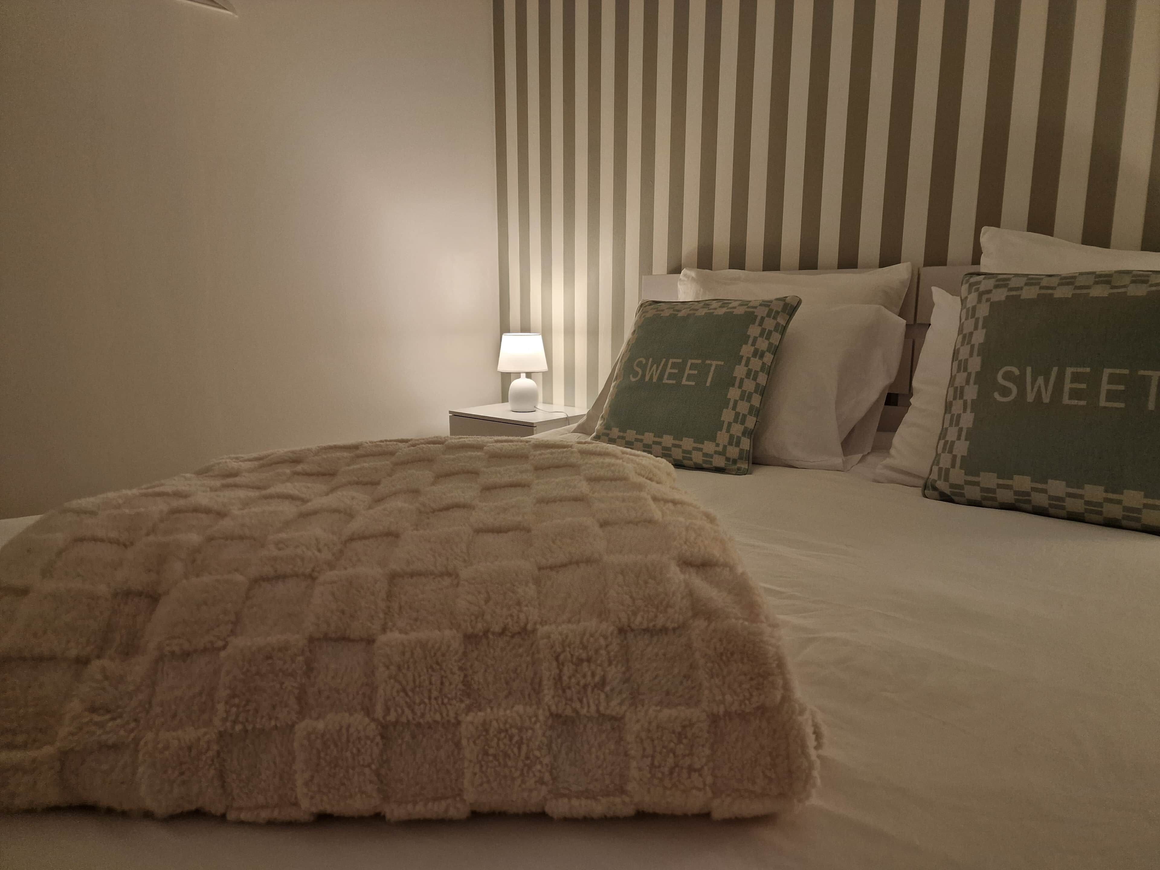 A hotel room with a bed, pillows, a nightstand, and a lamp.