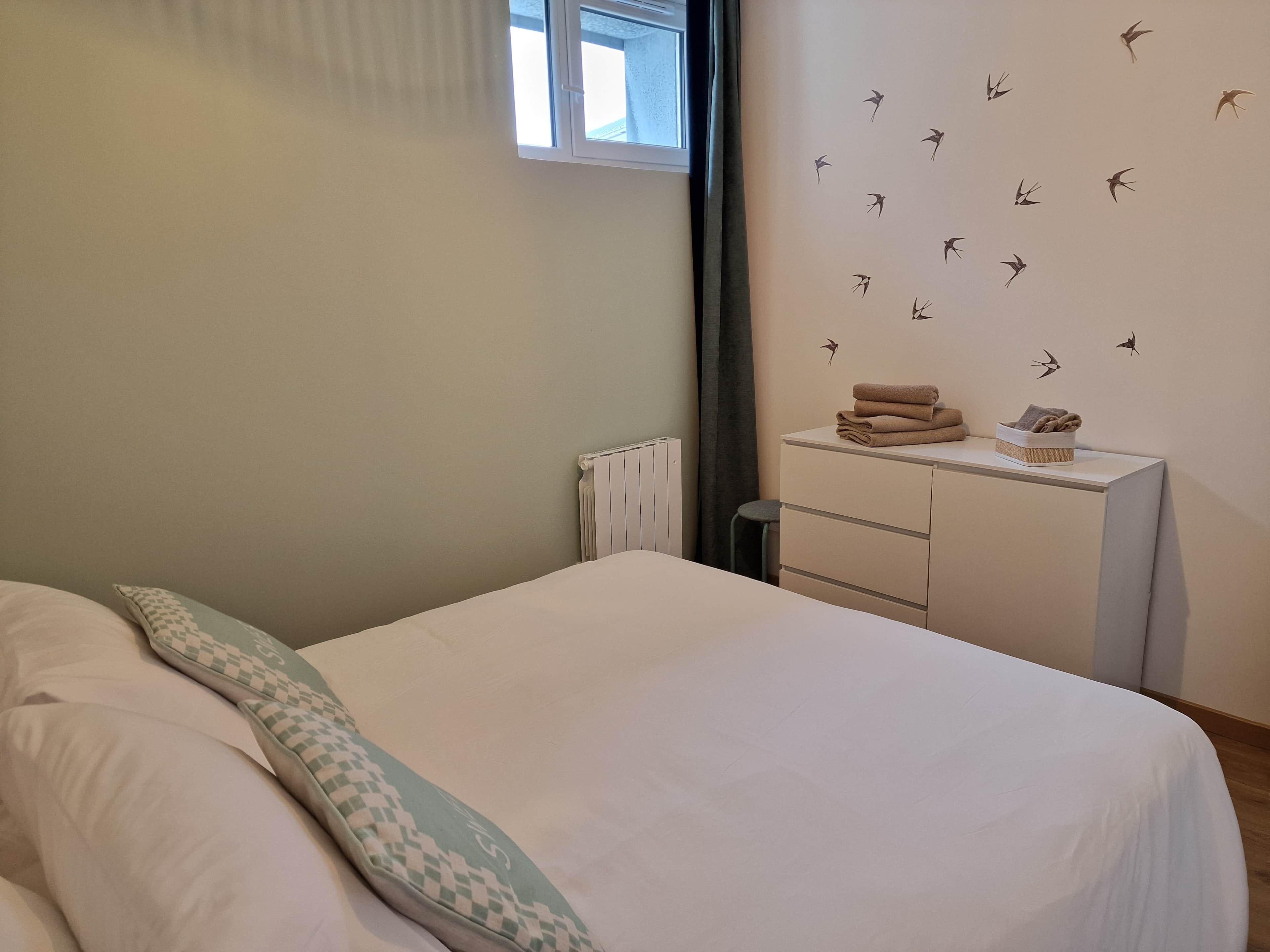 A bedroom with a bed, a bedside table with towels, a radiator, and a wall with bird decals.