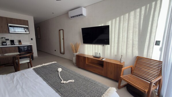 A modern hotel room with a bed, a wooden bench, a TV, a kitchenette, and a large window with blinds. - Family Pent-House with luxury amenities (Tulum)