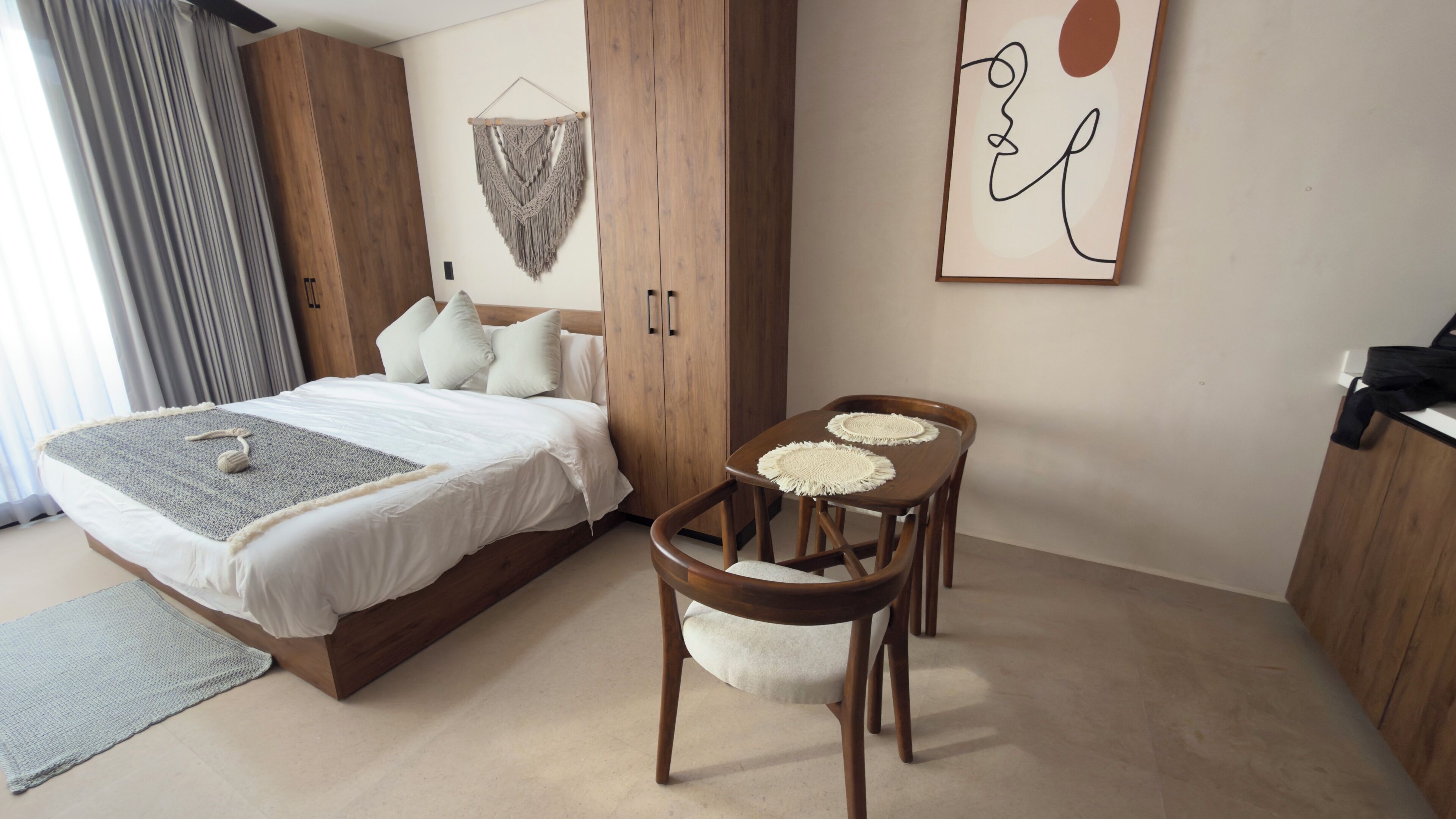 A bedroom with a bed, bedside table, chairs, a wooden wardrobe, and a wall art piece.