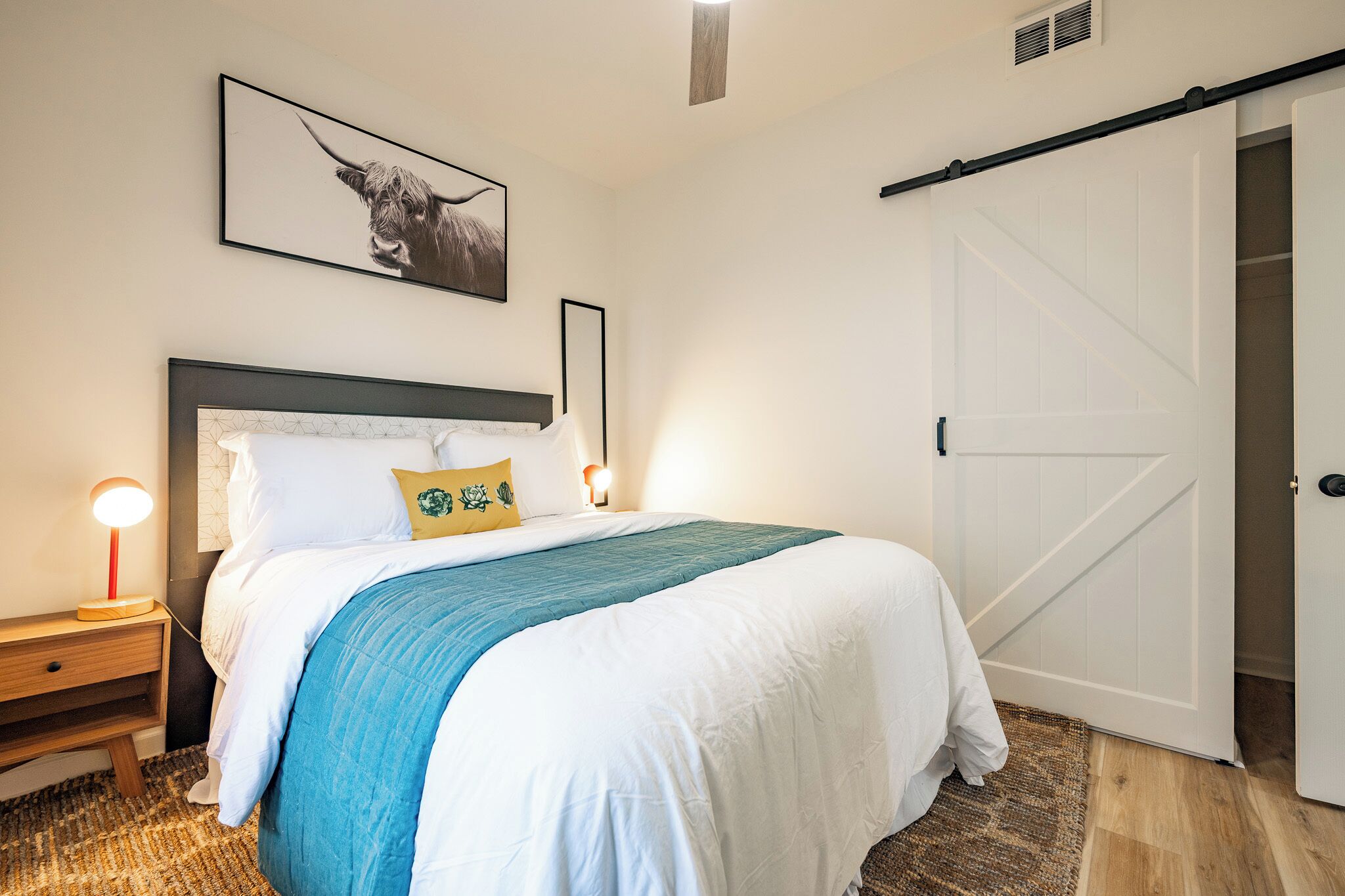Un dormitorio con cama, mesitas de noche, un cuadro en la pared, una puerta corredera y una alfombra con textura.