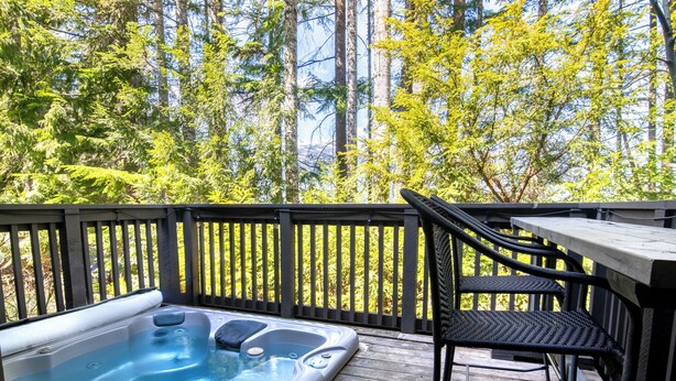 A hot tub on a wooden deck with a chair and a table, surrounded by trees. - Steller's Jay Chalet - private hot tub, ski in/out, 2 bedroom, 2 bath townhome (Whistler)