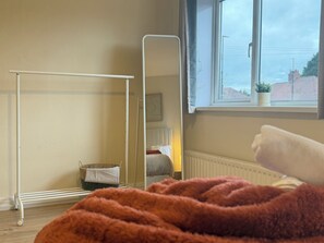 Ein Zimmer mit einem stehenden Spiegel, einem Heizkörper, einem Fenster mit Ausblick und einer Decke auf dem Boden.
