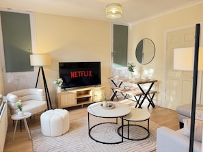 A living room with a TV displaying 'NETFLIX,' a sofa, a coffee table, a lamp, and a small side table with a plant. - Large 3 bed house, 4 TVs, driveway parking. (Newcastle upon Tyne)