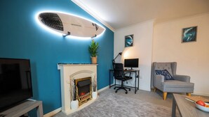 A living room with a fireplace, a flat-screen TV, a desk with a computer, and a comfortable armchair.