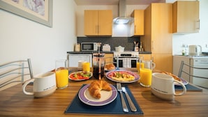 A breakfast table with croissants, plates of food, and glasses of orange juice in a modern kitchen with wooden cabinets and a microwave.