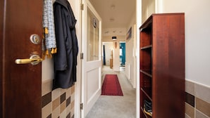 A hallway with a wooden door, a black coat hanging, a red carpet, and a blue wall in the distance.