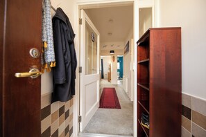 A hallway with a wooden door, a black coat hanging, a red carpet, and a blue wall in the distance. - Surfer 2Bed GF Flat Central Thurso, Parking, Full Fibre, Workspace, Pet friendly (Thurso)
