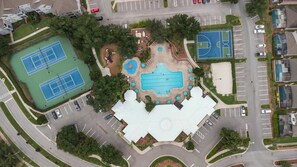 Ett flygbildsbild av ett bostadsområde med en swimmingpool, tennisbanor och en parkeringsplats.