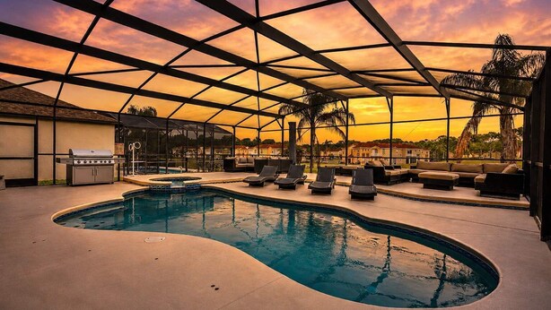 Zona de piscina con sillones de descanso, una parrilla y vista al atardecer.