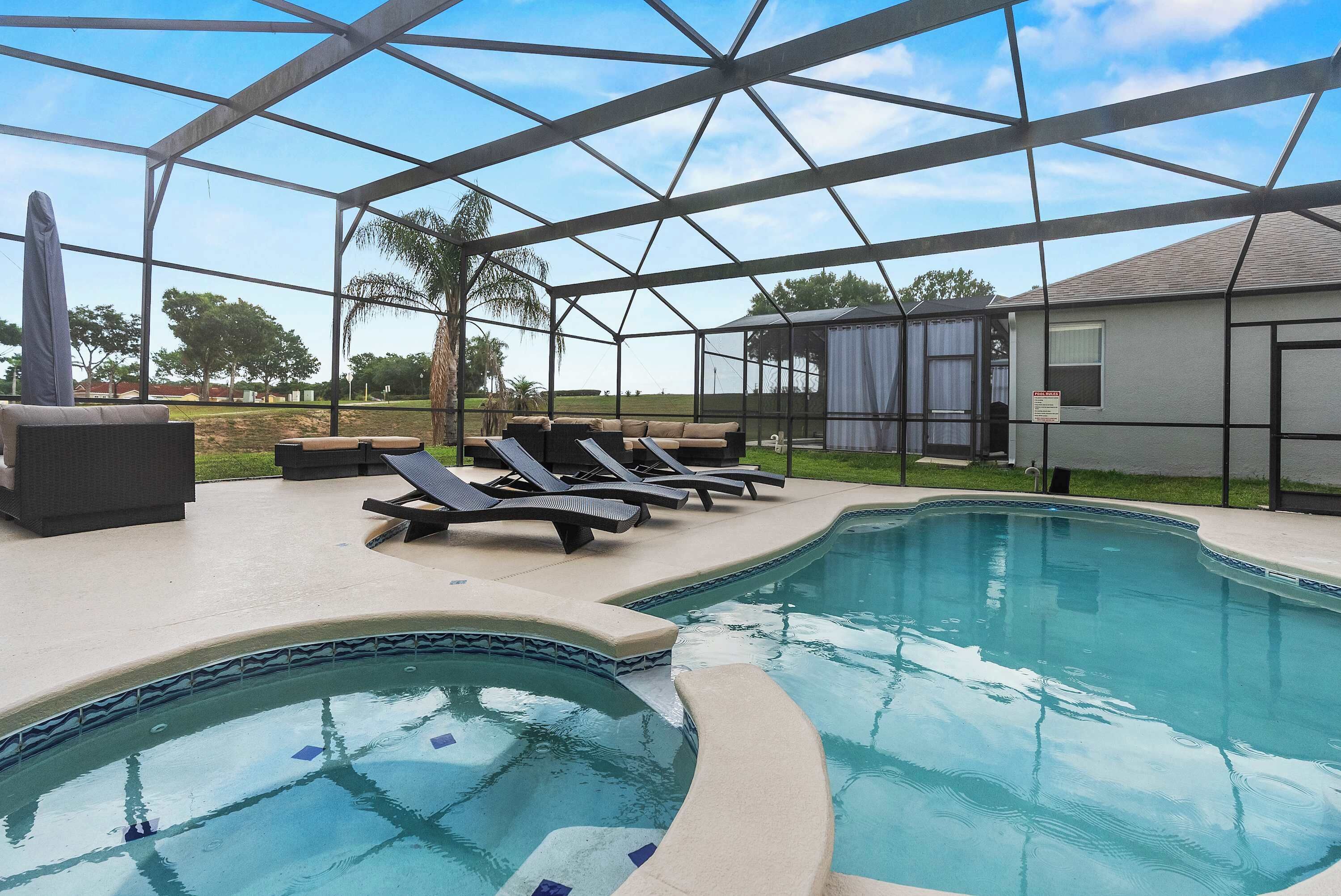 A swimming pool with a curved edge, surrounded by lounge chairs and a covered area with a metal frame.