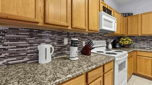 Una cocina con armarios de madera, un microondas blanco, una estufa, una cafetera y un bloque de cuchillos.