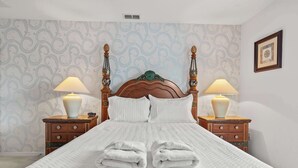 Una cama bien hecha con sábanas blancas, dos mesitas de noche con lámparas y un papel tapiz estampado.