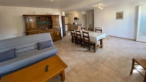Ein Wohnzimmer mit einer Couch, einem Esstisch mit Stühlen, einer Küchenzeile und einem großen Fenster.